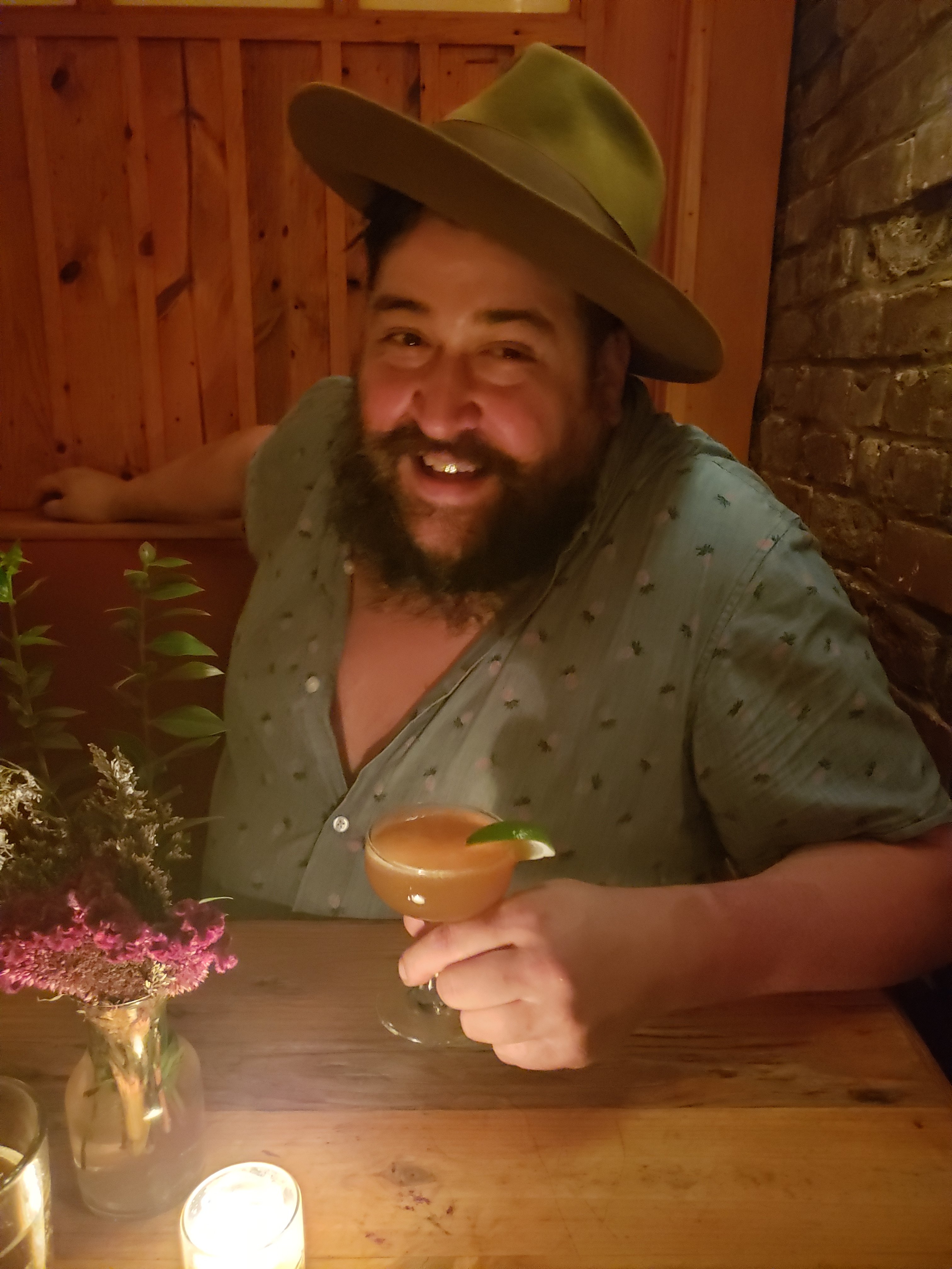 Hat-wearing guest smiling with a cocktail at Love & Exile, Nashville